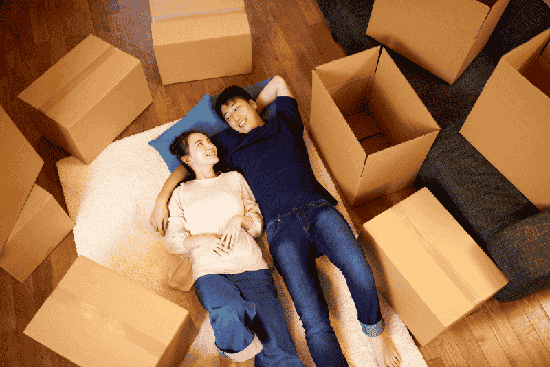 Homem e mulher sorriedentes deitados em meio a caixas de mudança
