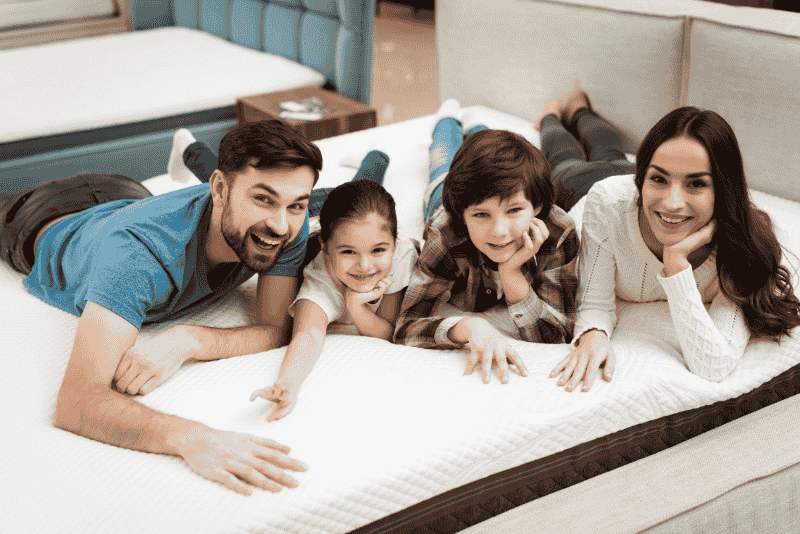 Untitled design (16) Família sorridente deidata no colchão