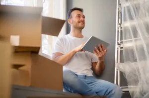 img_13 Homem sorridente com tablet em meio a caixas de mudança