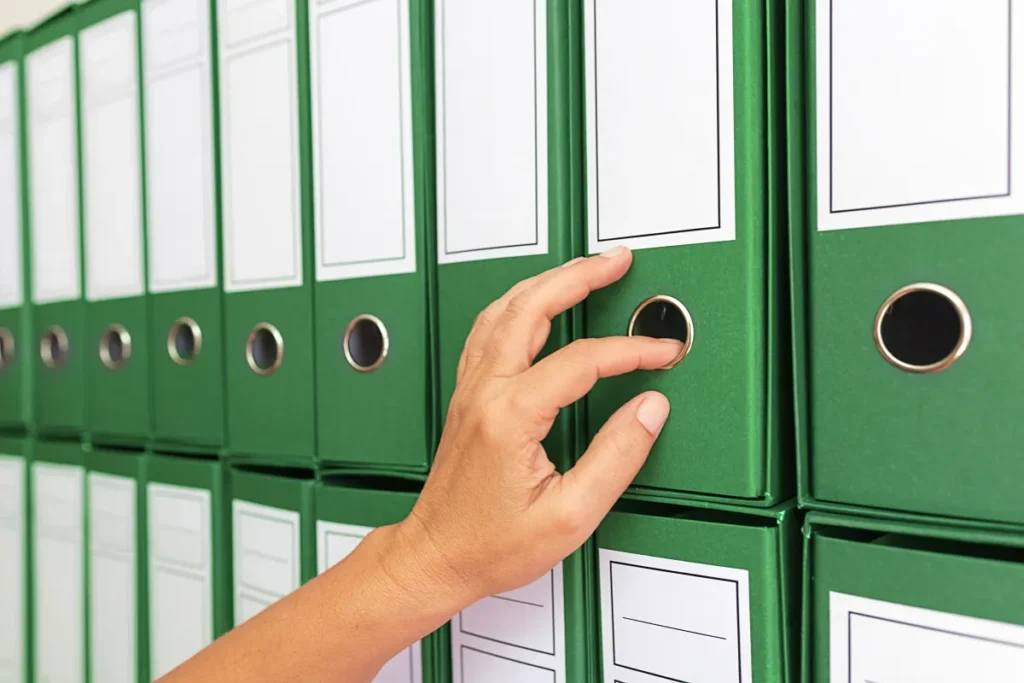 Mão segurando pasta de documentos em meio a outras pastas
