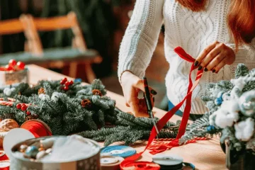 Mulher cortando fitas em mesa com vários itens de natal
