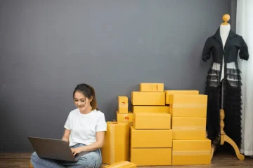 Jovem usando laptop em meio a caixas de pertences